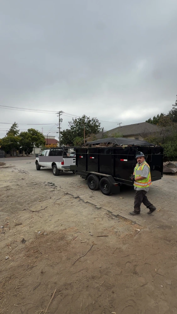 Pickup truck towing a full dump trailer, crew member walking alongside