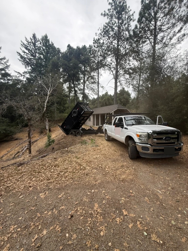 Pickup truck and dump trailer unloading on a wooded job site